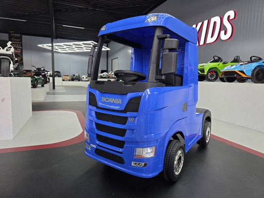 Carrello elettrico per bambini blu con volante e sedile, design realistico di camion Scania, in esposizione in showroom con auto giocattolo sullo sfondo