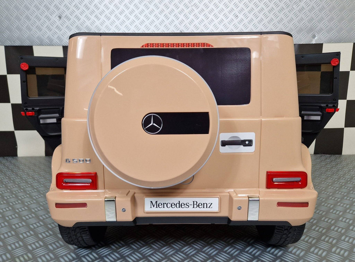 Auto elettrica per bambini Mercedes G500 colore sabbia con dettagli realistici, volante, luci LED e sedile in pelle, dimensioni compatte.