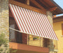 Tenda da sole a caduta a strisce rosse e bianche installata su balcone in esterno, struttura robusta per protezione solare e clima.