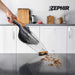 Aspiratutto portatile Zephir con manico ergonomico, in uso su superficie di cucina bianca, con polvere e detriti visibili sotto.