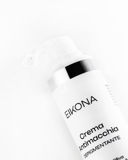 Applicazione di crema viso depigmentante Eikona, con crema bianca cremosa che fuoriesce dal contenitore, sfondo bianco minimalista