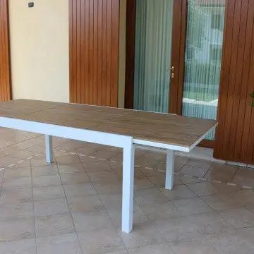 Tavolo da giardino Cayman allungabile posizionato su terrazza, struttura in alluminio bianco e piano effetto legno teak