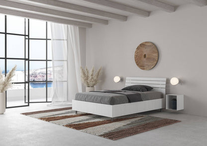 Letto singolo Ankel bianco con contenitore, posizionato in una camera con ampie finestre e decorazioni naturali.