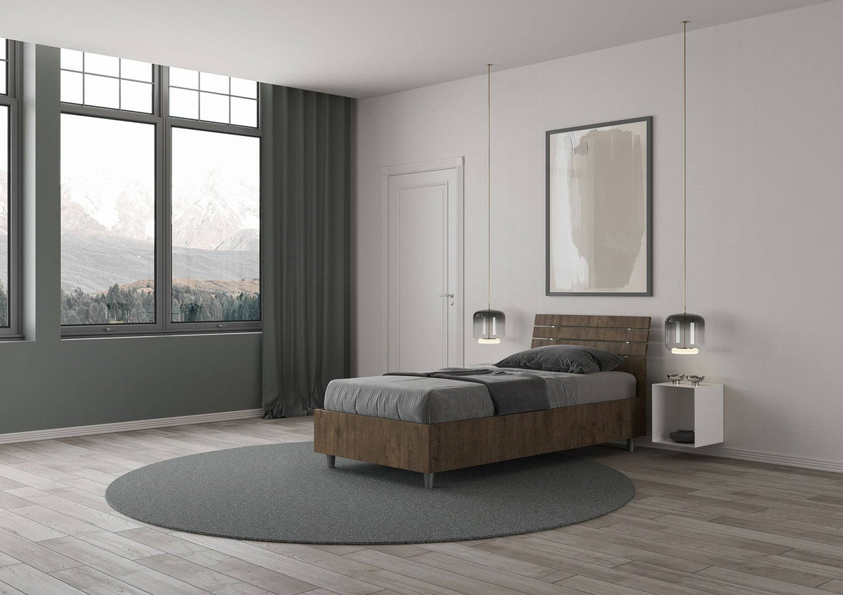 Letto singolo Ankel effetto legno scuro con contenitore, posizionato in una camera con ampie finestre e vista panoramica.