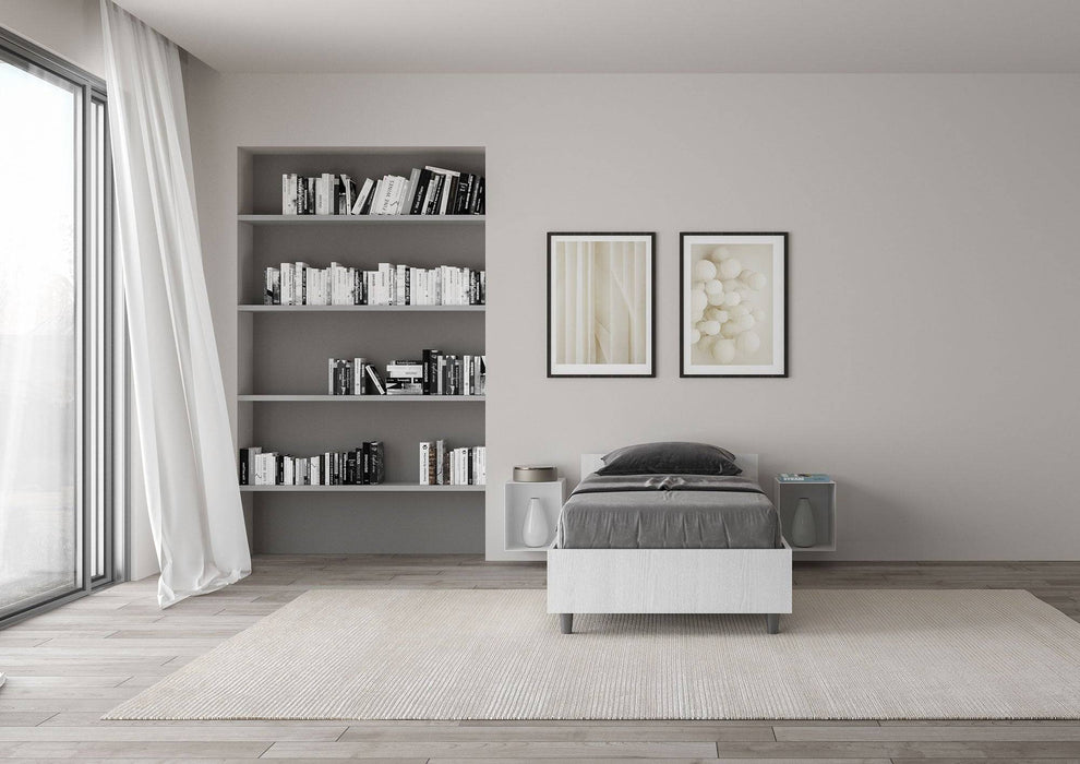 Letto singolo 80x190 Nuamo bianco in una stanza luminosa con libreria e decorazioni eleganti, design essenziale e pratico.