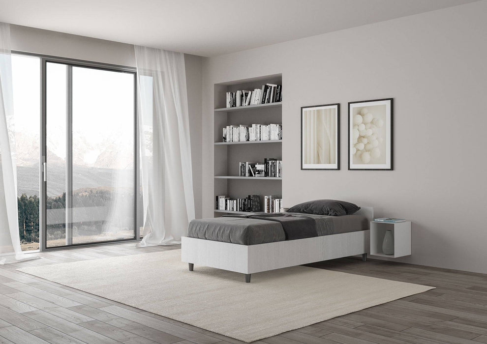 Letto singolo Nuamo bianco con rete contenitore in una camera moderna con ampie finestre e libreria integrata.