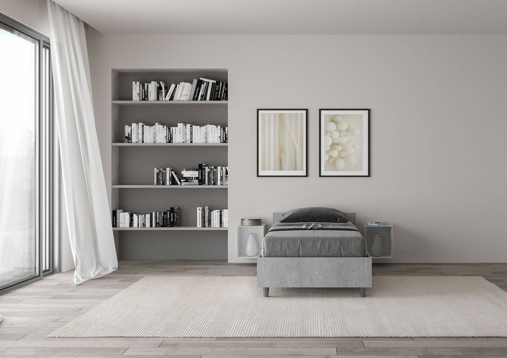Letto singolo 80x190 Nuamo effetto cemento in una stanza luminosa con libreria e decorazioni eleganti, design pratico.