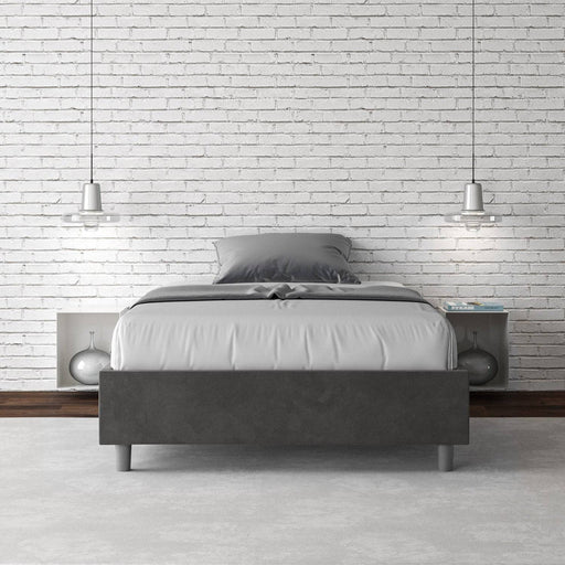 Letto singolo contenitore imbottito 100x210 microfibra Azelia grigio scuro in camera moderna con parete in mattoni bianchi e illuminazione sospesa.