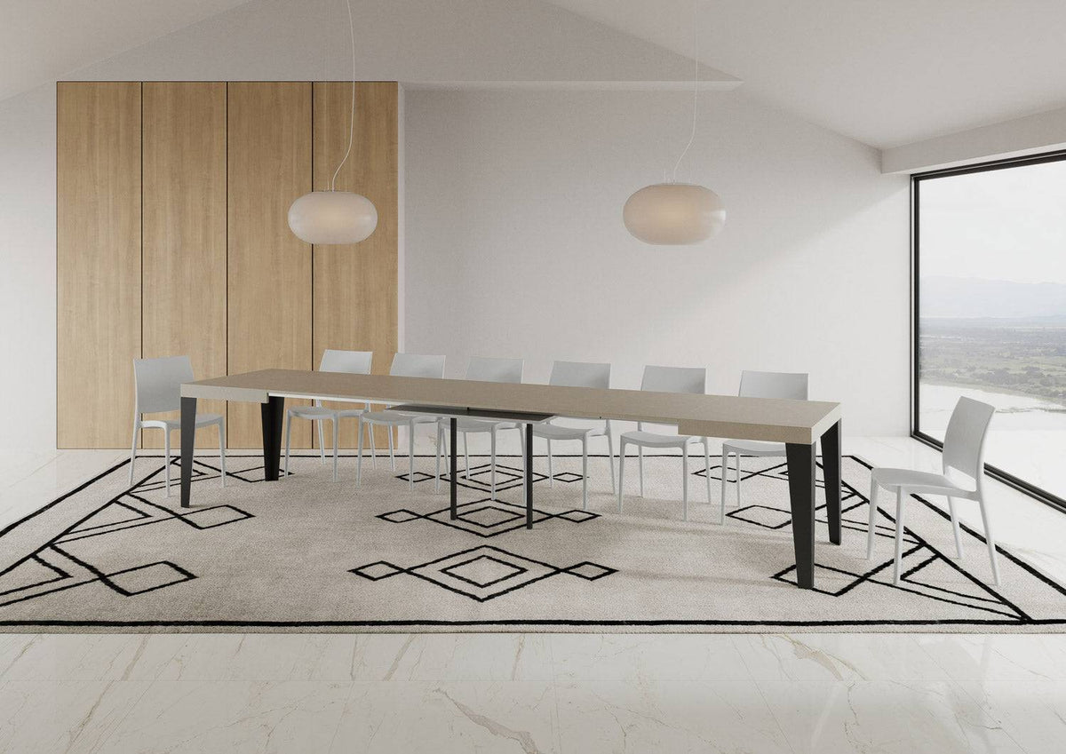 Tavolo Flame allungabile con gambe antracite, completamente esteso in sala da pranzo moderna con sedie bianche e tappeto chiaro.
