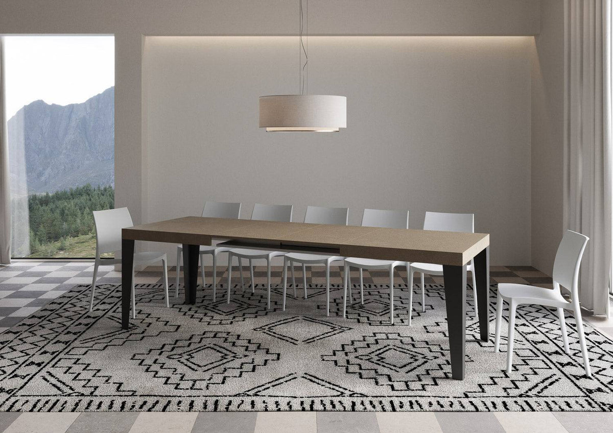 Tavolo Flame allungabile con gambe antracite, completamente esteso per 18 persone in ambiente elegante con tappeto geometrico.