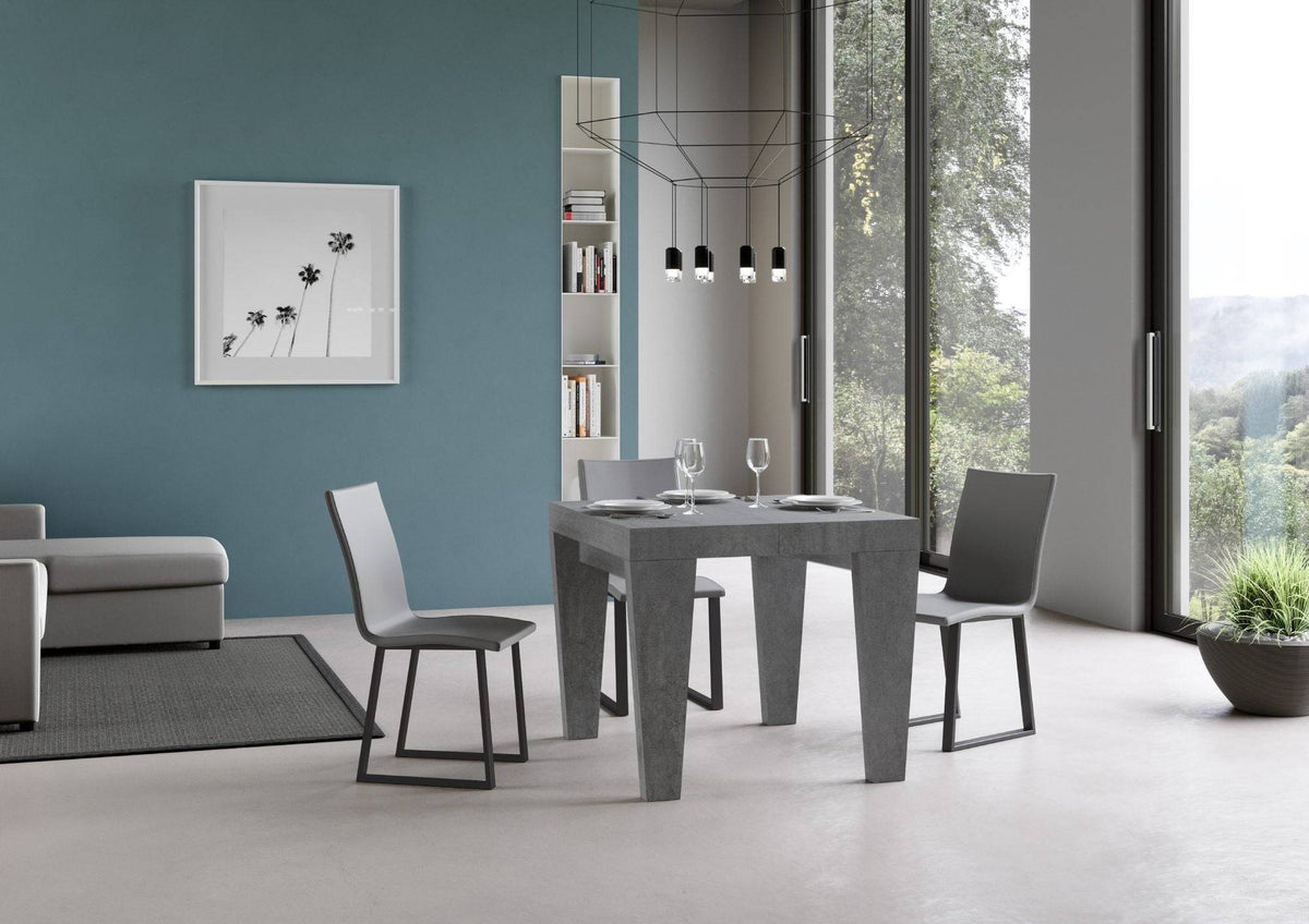 Tavolo allungabile Spimbo in finitura cemento scuro in versione compatta, abbinato a sedie moderne in soggiorno elegante.