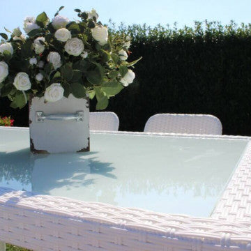 Dettaglio del piano in vetro del tavolo Azore bianco, decorato con un vaso di fiori, perfetto per pranzi all'aperto.