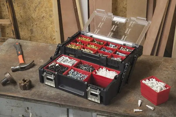 Cassetta organizer cantilever 22p Keter aperta su banco da lavoro, con vassoi estraibili pieni di viti e tasselli, perfetta per ferramenta.