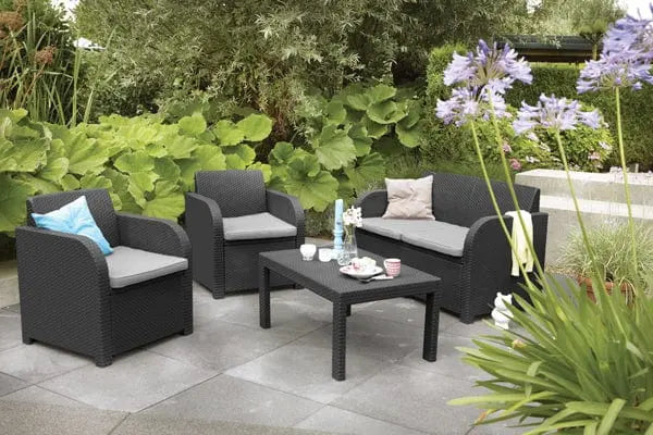 Salotto Carolina graphite con cuscini grigi da esterno, composto da divano, due poltrone e tavolino, su patio in giardino moderno